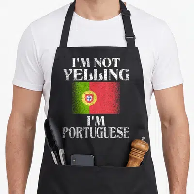 Yelling portuguese apron - Distressed white text I'M NOT YELLING I'M PORTUGUESE around green red flag — shown on a black cotton canvas apron against a white background