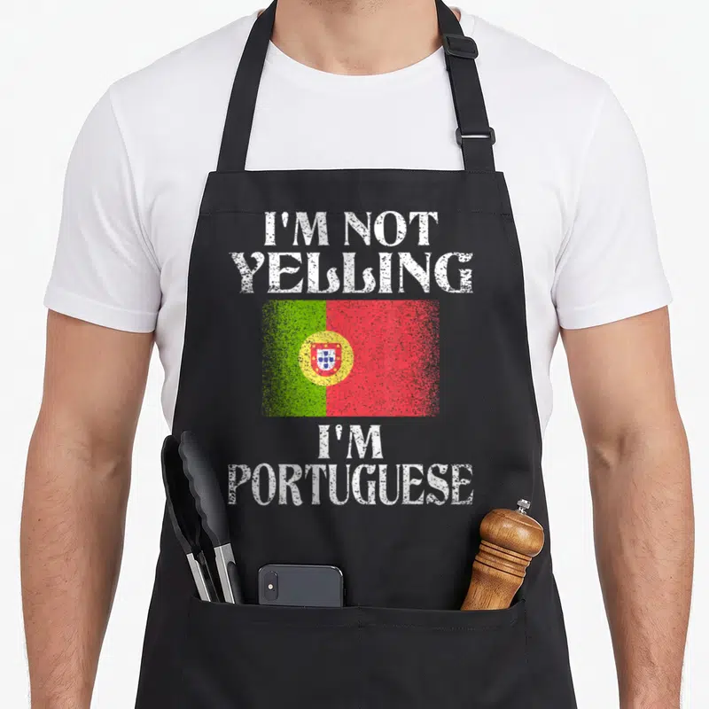 Yelling portuguese apron - Distressed white text I'M NOT YELLING I'M PORTUGUESE around green red flag — shown on a black cotton canvas apron against a white background