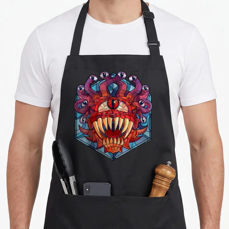 Beholder stained apron - Stained glass style monster head with tentacles and multiple eyes inside a blue hexagon — shown on a black cotton canvas apron against a white background
