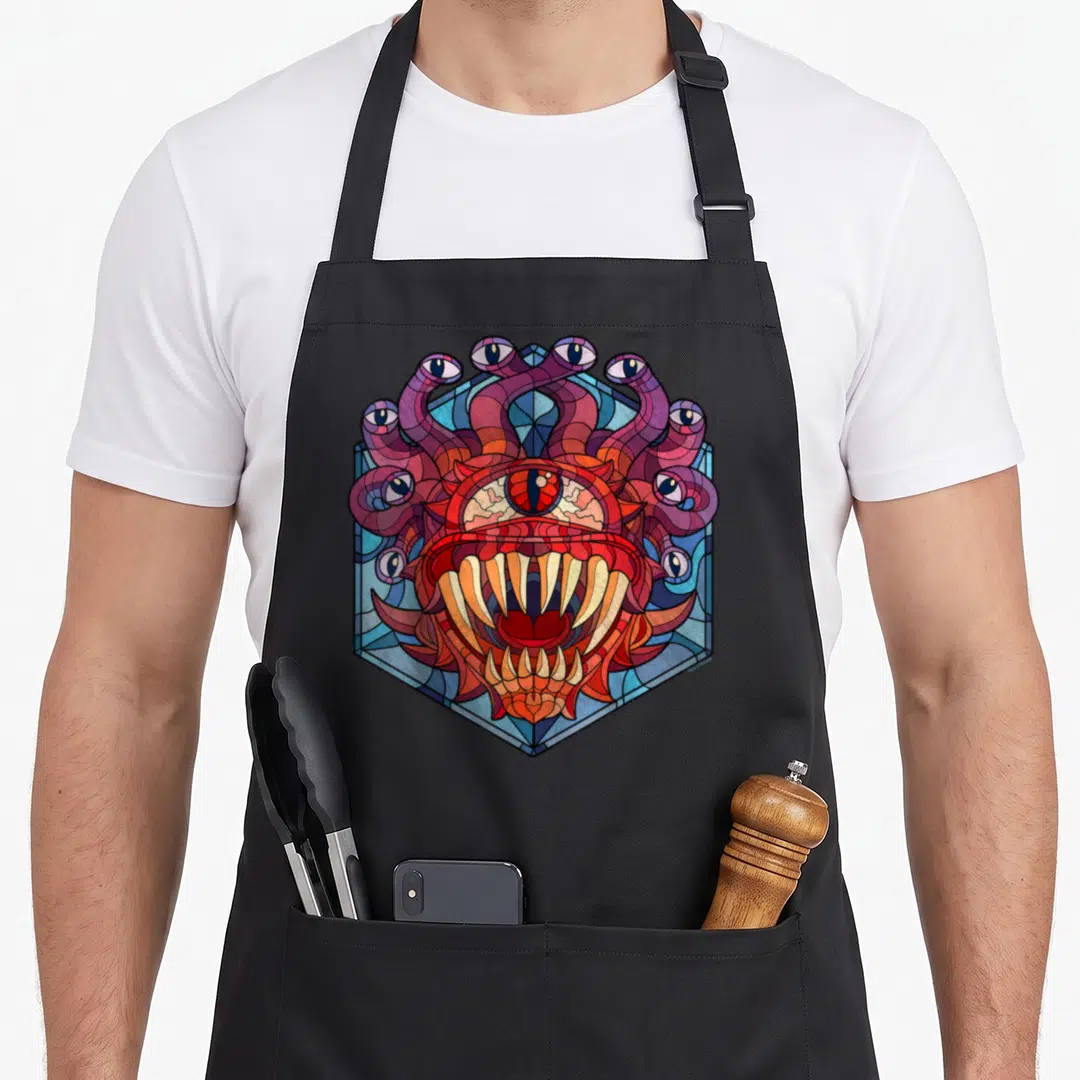Beholder stained apron - Stained glass style monster head with tentacles and multiple eyes inside a blue hexagon — shown on a black cotton canvas apron against a white background