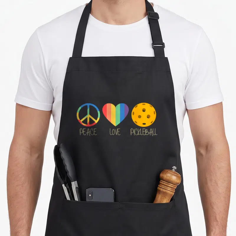 Funny peace pickleball apron - Three symbols: peace sign, heart, pickleball with tan text below — shown on a black cotton canvas apron against a white background