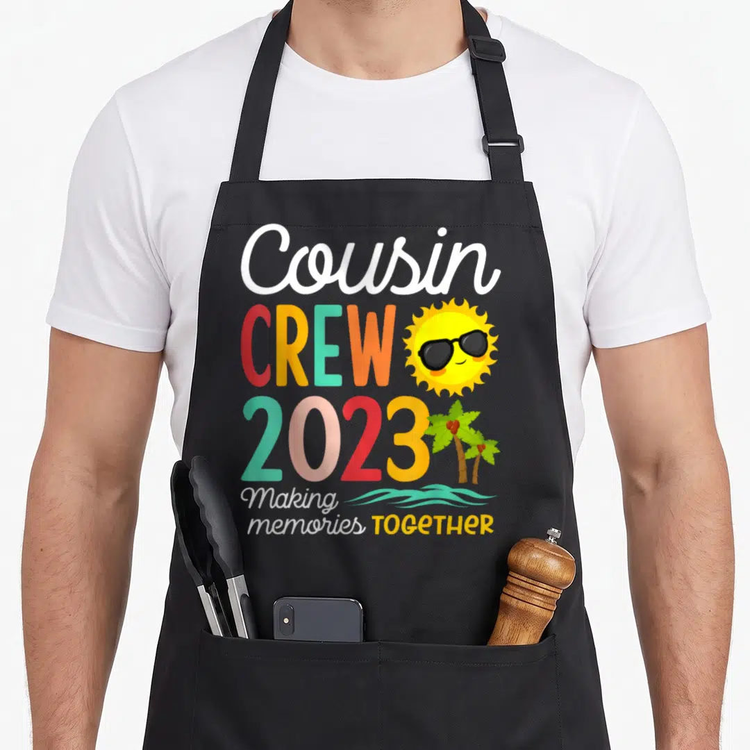 Cousin crew family aprons - Cousin CREW 2023 text with cartoon sun sunglasses palm trees and teal waves — shown on a black cotton canvas apron against a white background