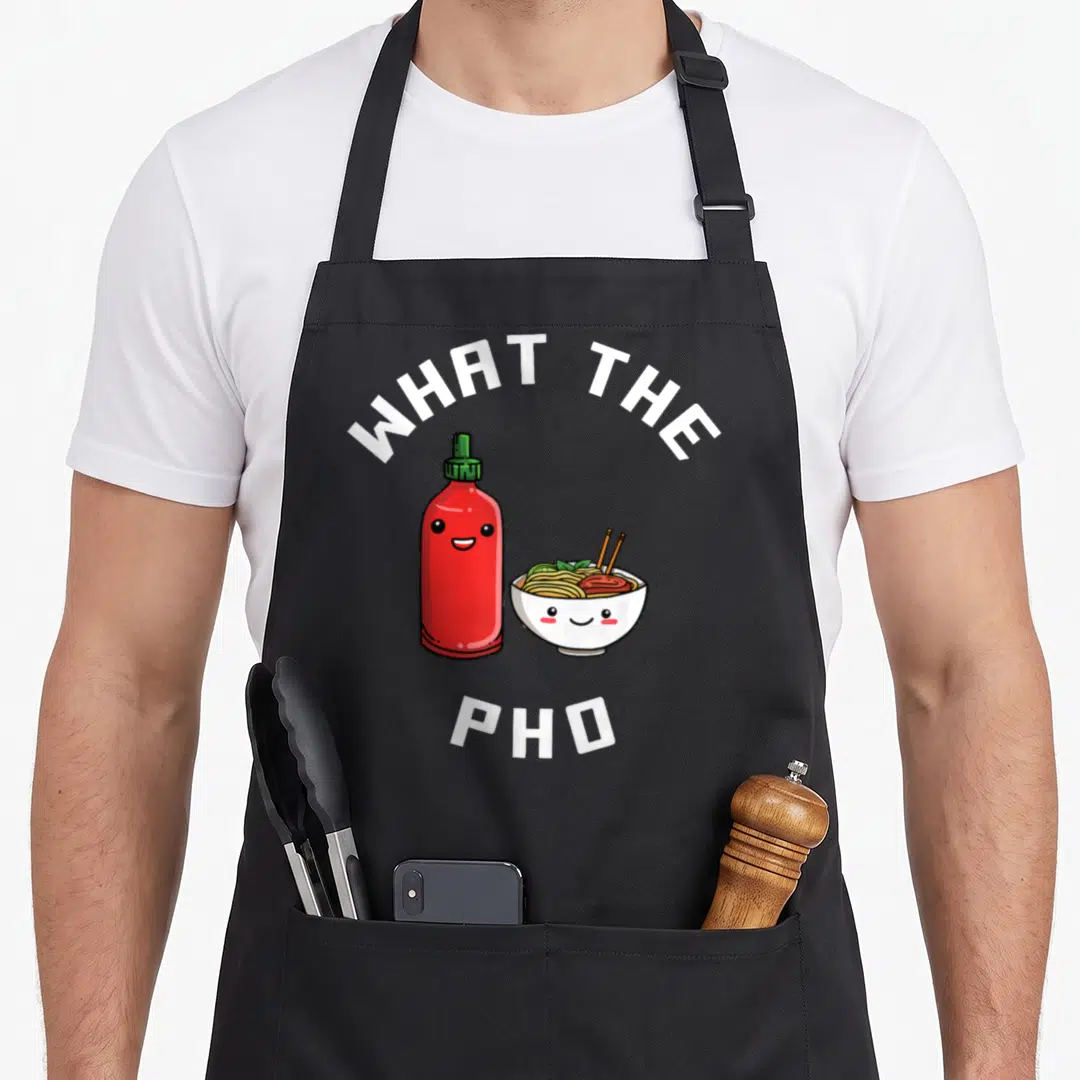 Food pho apron - Cartoon sriracha bottle and pho bowl with text WHAT THE PHO in white, red, yellow, green — shown on a black cotton canvas apron against a white background