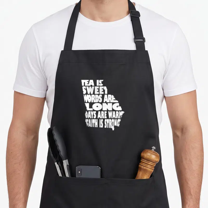 Tea pride apron - White text forming Georgia state shape with Southern phrases on black apron — shown on a black cotton canvas apron against a white background