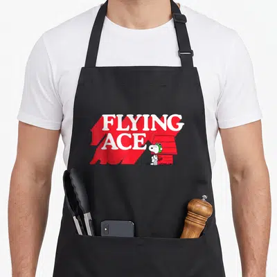 Ace flying apron - FLYING ACE text with red shadow, cartoon dog in green helmet, and red doghouse — shown on a black cotton canvas apron against a white background
