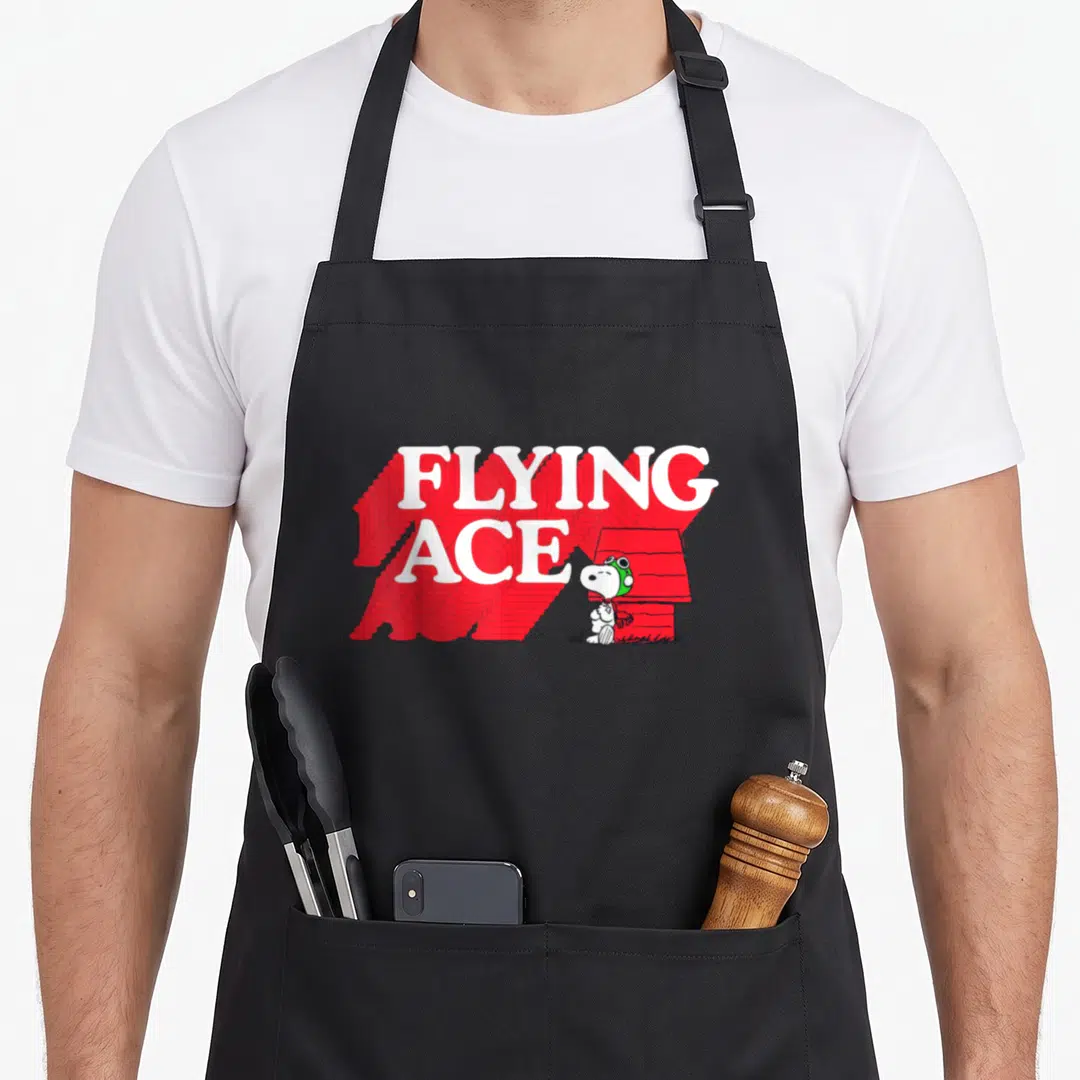 Ace flying apron - FLYING ACE text with red shadow, cartoon dog in green helmet, and red doghouse — shown on a black cotton canvas apron against a white background