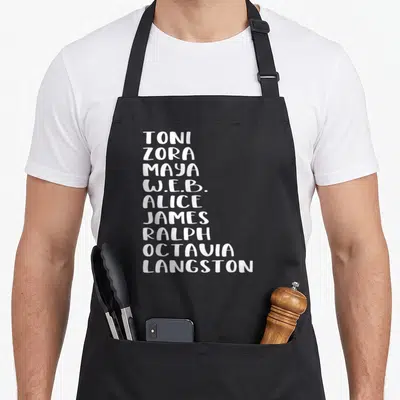 Famous african american aprons - Stacked white first names of Toni, Zora, Maya, W.E.B., Alice, James, Ralph, Octavia — shown on a black cotton canvas apron against a white background