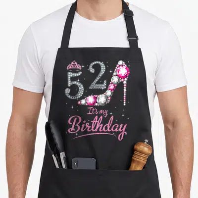 Nana queen apron - 52 high heel shoe pink birthday text crown illustration — shown on a black cotton canvas apron against a white background