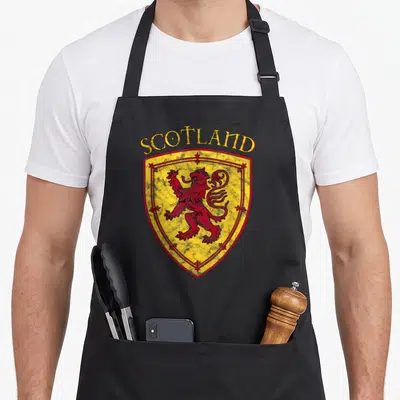 Arm lion apron - Red lion rampant on yellow shield with arched SCOTLAND text in distressed style — shown on a black cotton canvas apron against a white background