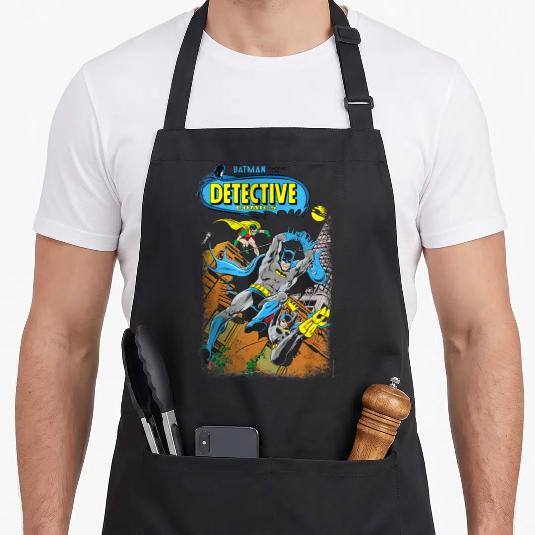 Funny detective apron - Comic cover art with Batman Robin and Batgirl swinging above buildings in blue yellow grey — shown on a black cotton canvas apron against a white background