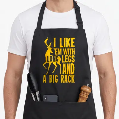 Deer grill hunter apron - Yellow distressed deer silhouette with stacked text I LIKE 'EM WITH LONG LEGS AND A BIG RACK — shown on a black cotton canvas apron against a white background