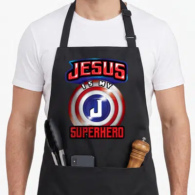 Powerful christian apron - Red white and blue shield with JESUS IS MY SUPERHERO text and white J logo — shown on a black cotton canvas apron against a white background