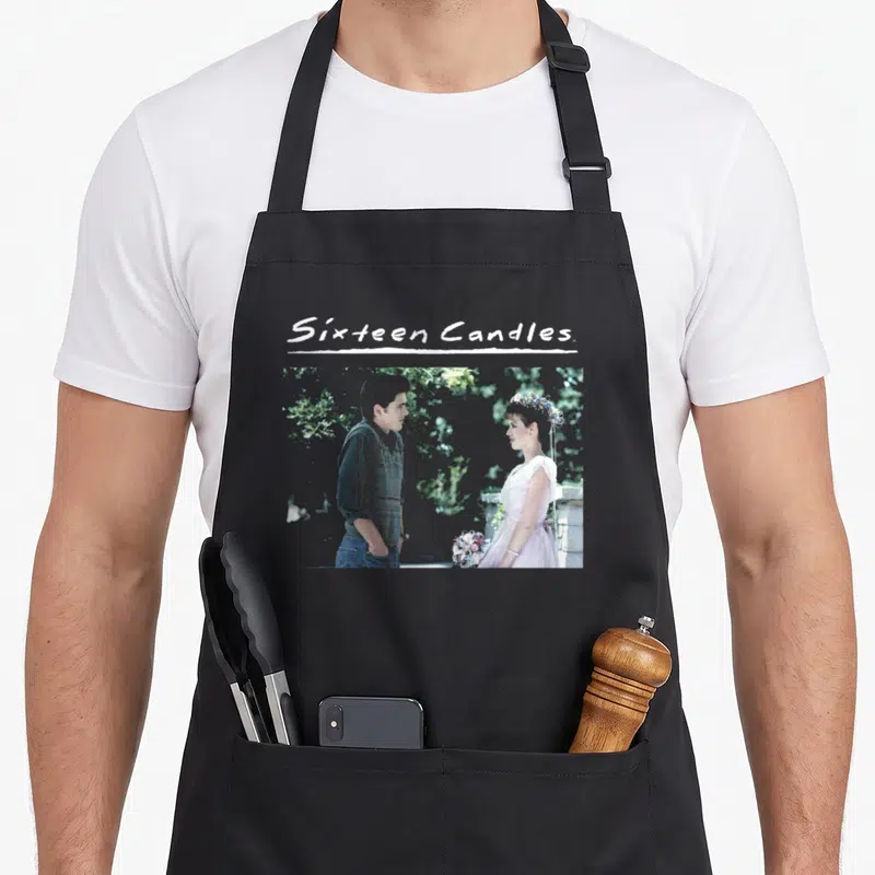 Sixteen wedding apron - Sixteen Candles text above photo of couple in pink dress and grey shirt — shown on a black cotton canvas apron against a white background