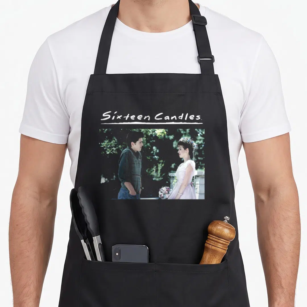 Sixteen wedding apron - Sixteen Candles text above photo of couple in pink dress and grey shirt — shown on a black cotton canvas apron against a white background