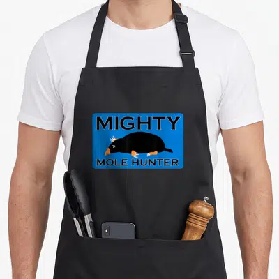 Mole hunter apron - Blue rectangle with Mighty Mole Hunter text and dead cartoon mole illustration — shown on a black cotton canvas apron against a white background