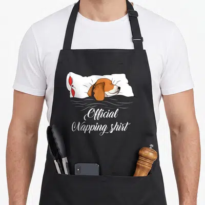 Sleeping beagle apron - Cartoon beagle sleeping on pillow with Official Napping Shirt text — shown on a black cotton canvas apron against a white background