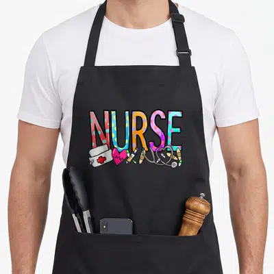 Week nurse apron - Colorful NURSE text with cartoon hat, heart, syringe, stethoscope, and pills — shown on a black cotton canvas apron against a white background