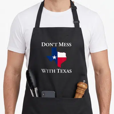 Mess texas apron - DON'T MESS WITH TEXAS text framing a Texas state map in blue, white, and red flag colors — shown on a black cotton canvas apron against a white background