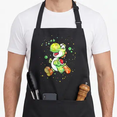 Splatter watercolor apron - Watercolor Yoshi running with green, orange, yellow, and red splatters — shown on a black cotton canvas apron against a white background