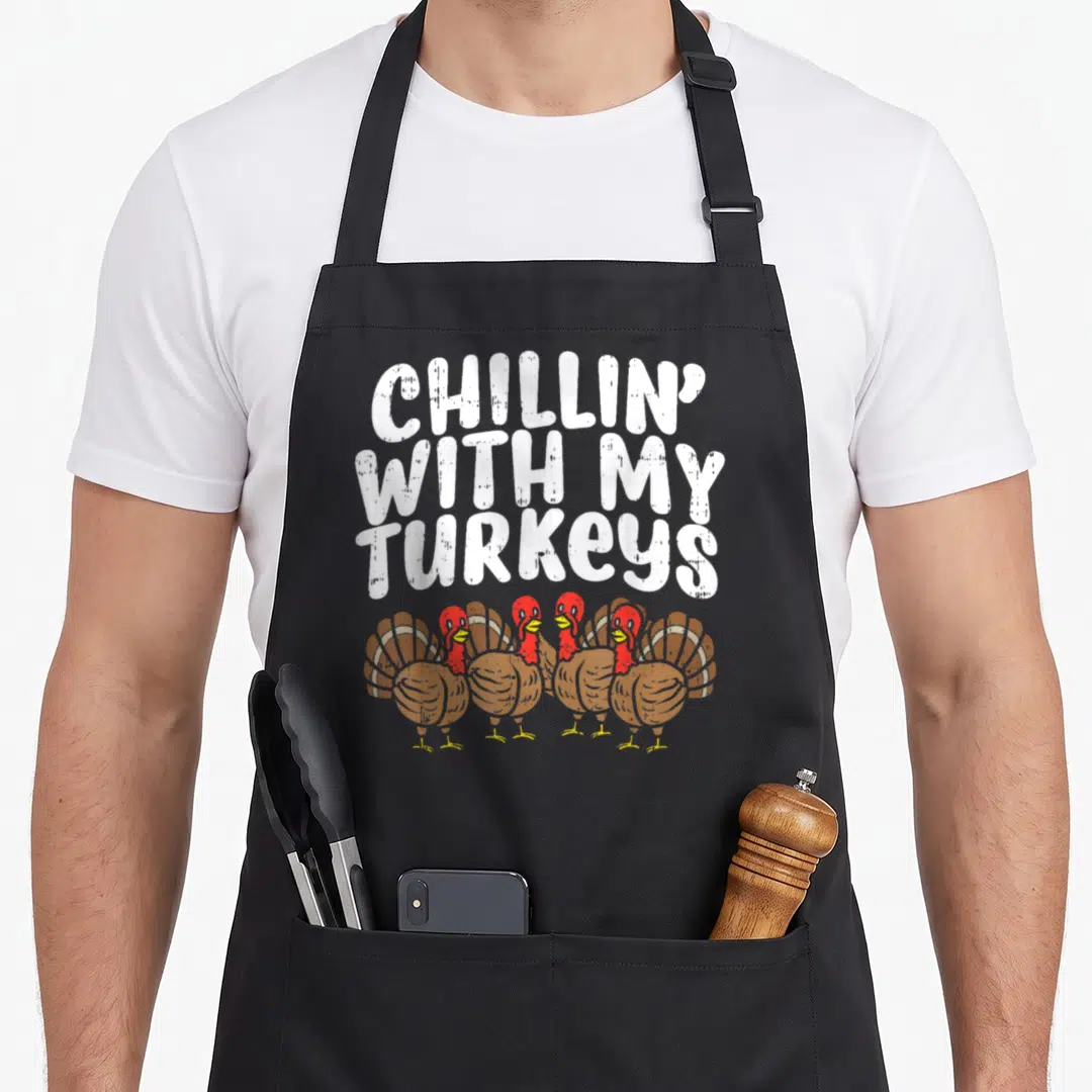 Chillin thanksgiving aprons - Three lines of white text above four cartoon turkeys with red heads and brown feathers — shown on a black cotton canvas apron against a white background