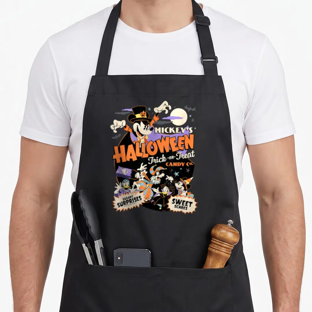 Halloween cotton candy apron - Mickey Mouse in top hat with orange Halloween text and costumed friends under a moon — shown on a black cotton canvas apron against a white background