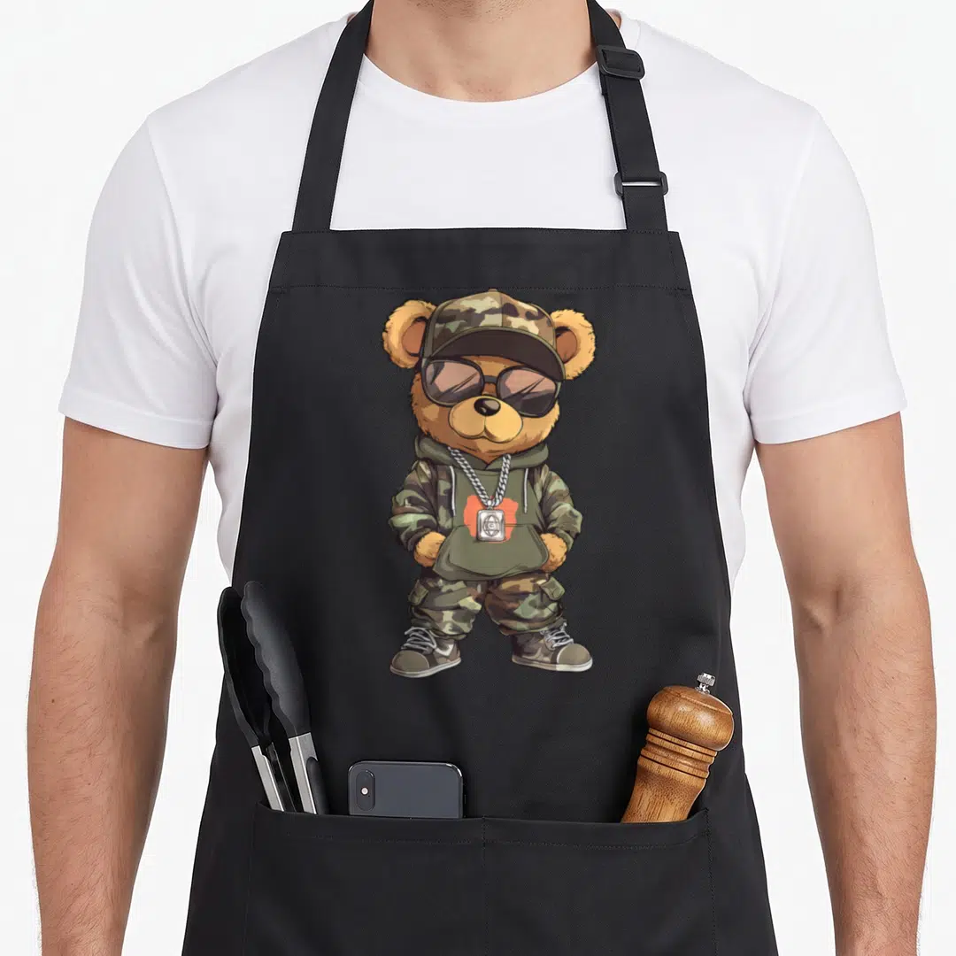Teddy hip apron - Cartoon bear in camo hoodie, sunglasses, and silver chain necklace — shown on a black cotton canvas apron against a white background