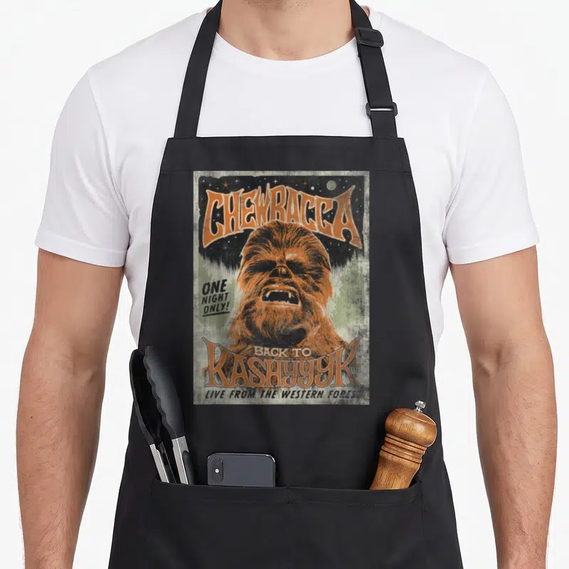 Funny kashyyyk concert apron - Retro concert poster design of Chewbacca with orange text and distressed green background — shown on a black cotton canvas apron against a white background