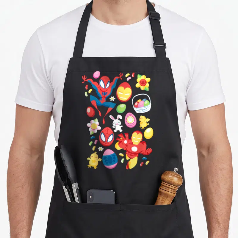 Vintage easter basket apron - Spider-Man Iron Man Easter eggs bunnies chicks jelly beans cartoon print — shown on a black cotton canvas apron against a white background