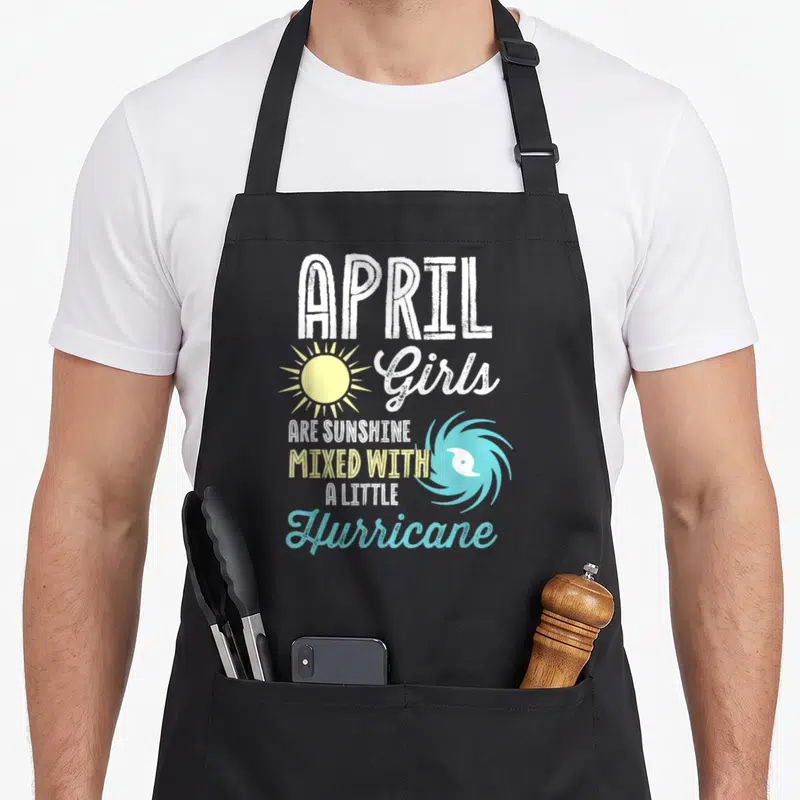 April sunshine birthday apron - Stacked white yellow blue text reading APRIL Girls Are Sunshine Mixed With A Little — shown on a black cotton canvas apron against a white background