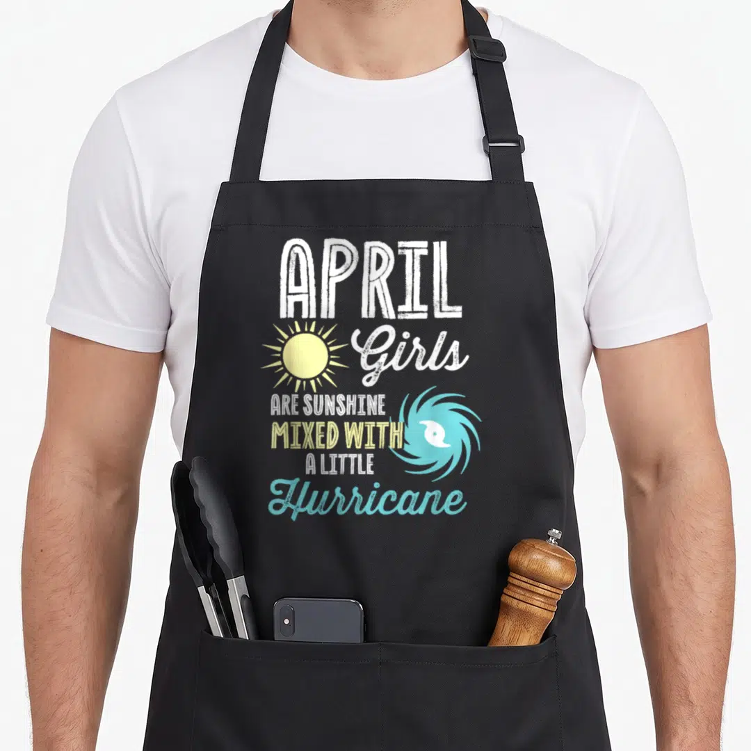 April sunshine birthday apron - Stacked white yellow blue text reading APRIL Girls Are Sunshine Mixed With A Little — shown on a black cotton canvas apron against a white background