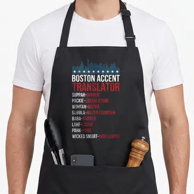 Accent wicked apron - Blue skyline and stars above a list translating Boston slang terms like Suppah and Packie — shown on a black cotton canvas apron against a white background