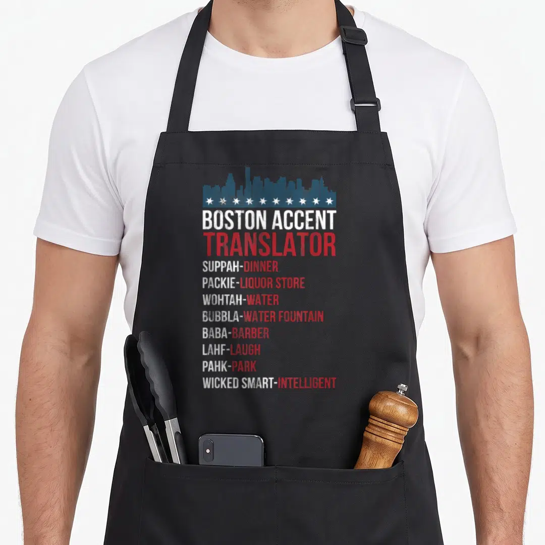 Accent wicked apron - Blue skyline and stars above a list translating Boston slang terms like Suppah and Packie — shown on a black cotton canvas apron against a white background