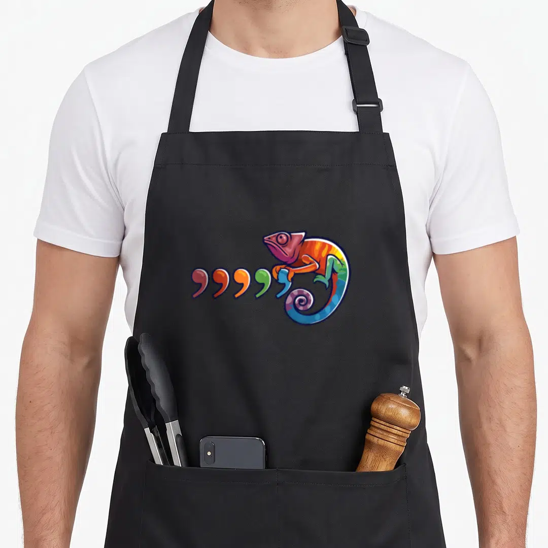 Comma 80s apron - Multicolored chameleon holding five commas in purple orange yellow green blue — shown on a black cotton canvas apron against a white background