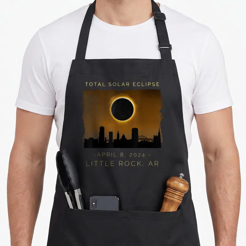 Total arkansas girl apron - Gold text Total Solar Eclipse over orange sky and black Little Rock skyline — shown on a black cotton canvas apron against a white background