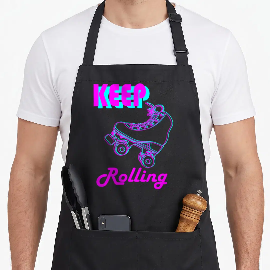 Rolling 80s apron - Magenta and cyan roller skate with KEEP Rolling text in retro style — shown on a black cotton canvas apron against a white background
