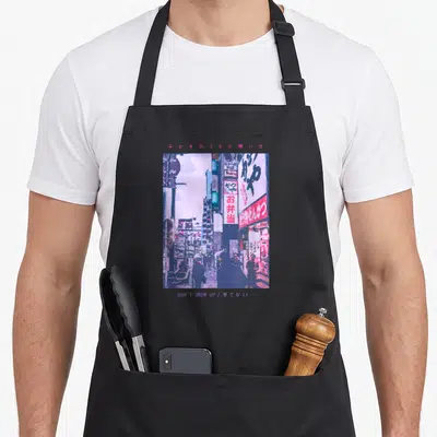 Tokyo streetwear apron - Pixelated city street scene in purple and pink with Japanese text and English phrase — shown on a black cotton canvas apron against a white background