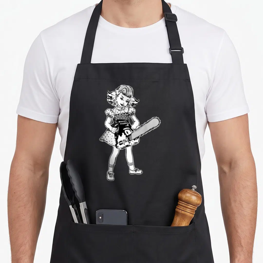 Fan goth apron - Cartoon girl in polka dot dress holding chainsaw in black white and grey — shown on a black cotton canvas apron against a white background