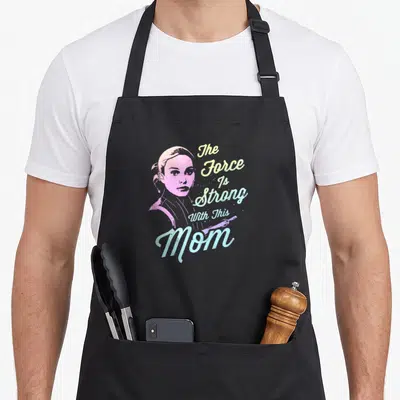 Padme mothers day apron - Pink woman portrait with The Force Is Strong With This Mom text and diagonal lightsaber — shown on a black cotton canvas apron against a white background