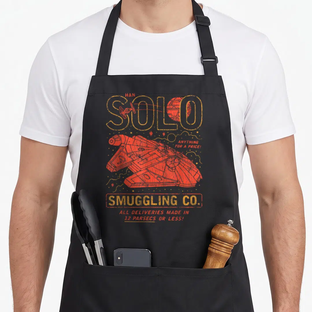 Smuggling star apron - Vintage Han Solo text with red Millennium Falcon and Smuggling Co logo on grey background — shown on a black cotton canvas apron against a white background