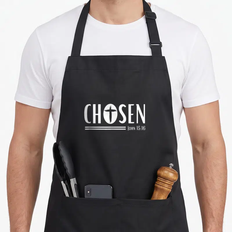 Chosen streetwear apron - White text CHOSEN with cross in O and John 15:16 verse below lines — shown on a black cotton canvas apron against a white background