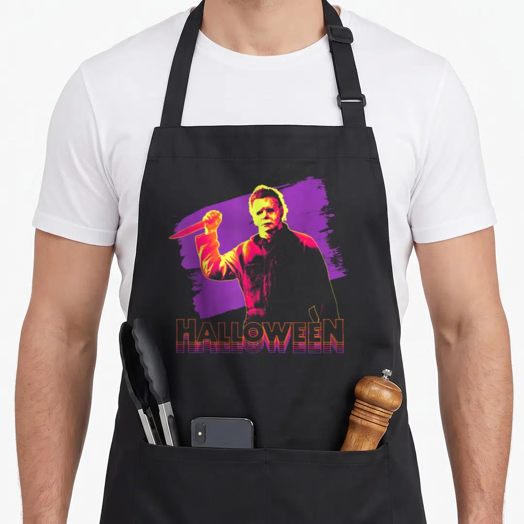 Neon halloween apron - Man holding knife over purple splash with 3D HALLOWEEN text in orange and purple — shown on a black cotton canvas apron against a white background