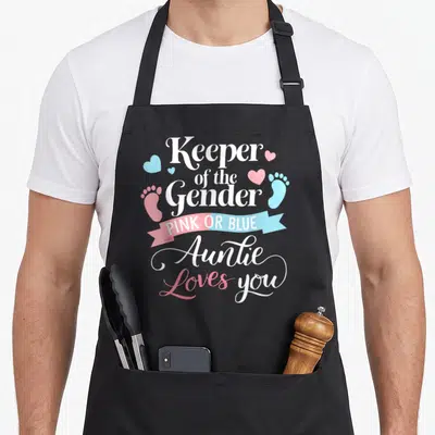 Gender aunt apron - White text Keeper of the Gender with pink and blue ribbons and footprints — shown on a black cotton canvas apron against a white background