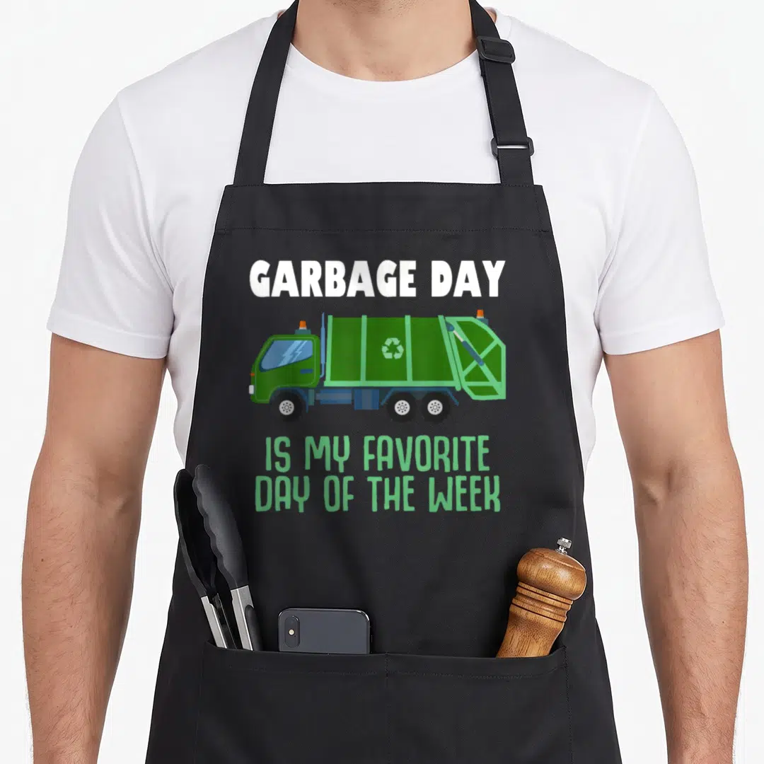 Trash truck apron - Green cartoon garbage truck with text GARBAGE DAY IS MY FAVORITE DAY OF THE WEEK — shown on a black cotton canvas apron against a white background