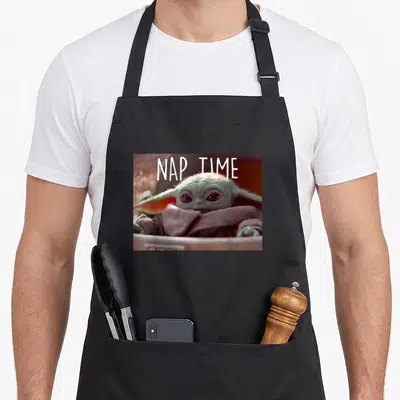 Cute nap apron - Grogu in pod with white NAP TIME text overlay — shown on a black cotton canvas apron against a white background