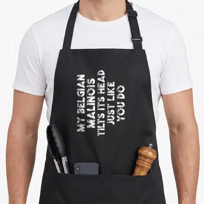 Funny belgian dog apron - White stacked text reading My Belgian Malinois Tilts Its Head Just Like You Do — shown on a black cotton canvas apron against a white background