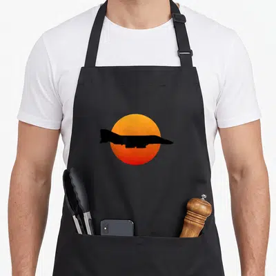 Phantom military apron - Black jet silhouette over orange and red circular sun, minimalist style — shown on a black cotton canvas apron against a white background