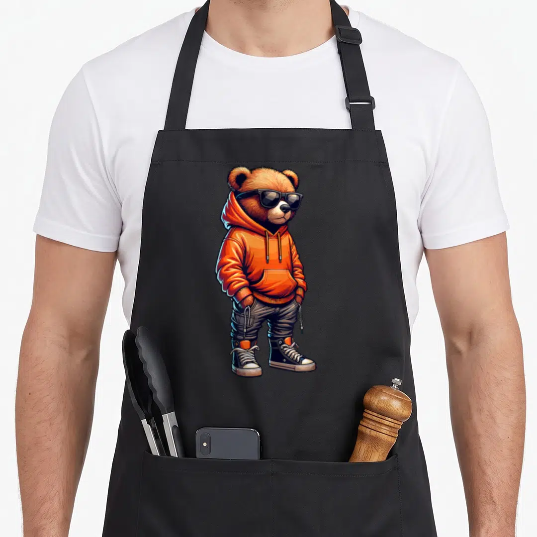 Teddy streetwear apron - Cartoon bear in orange hoodie, grey pants, sunglasses, and sneakers — shown on a black cotton canvas apron against a white background