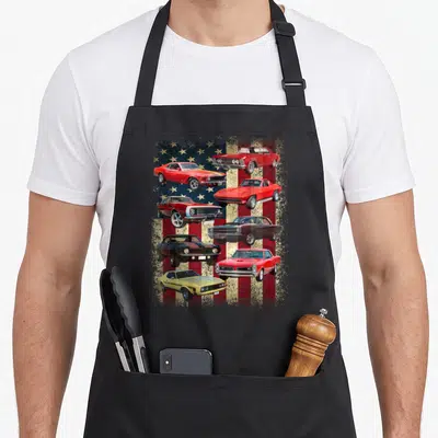 Flag muscle apron - Seven red white and blue muscle cars on distressed flag background — shown on a black cotton canvas apron against a white background