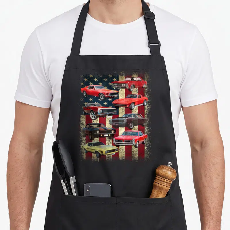 Flag muscle apron - Seven red white and blue muscle cars on distressed flag background — shown on a black cotton canvas apron against a white background