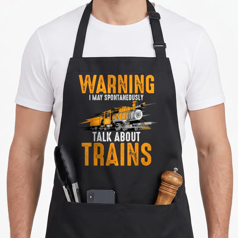 Warning talk apron - Orange cartoon steam train with lightning bolt and stacked warning text — shown on a black cotton canvas apron against a white background